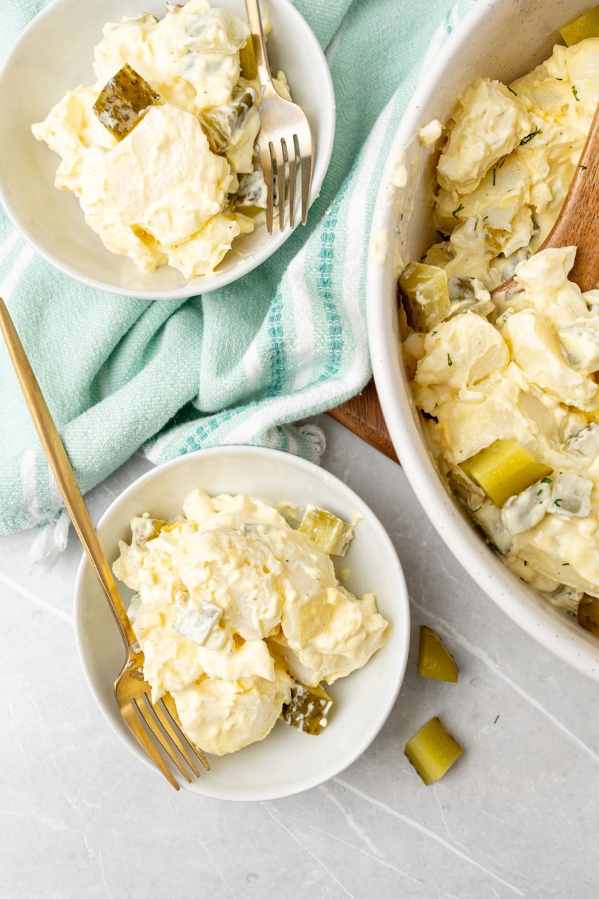 dill pickle potato salad in two small white bowls with gold forks resting on the sides