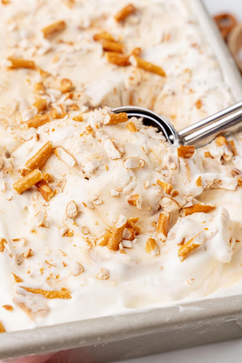 an ice cream scoop digging into a pan of no churn salted caramel pretzel ice cream