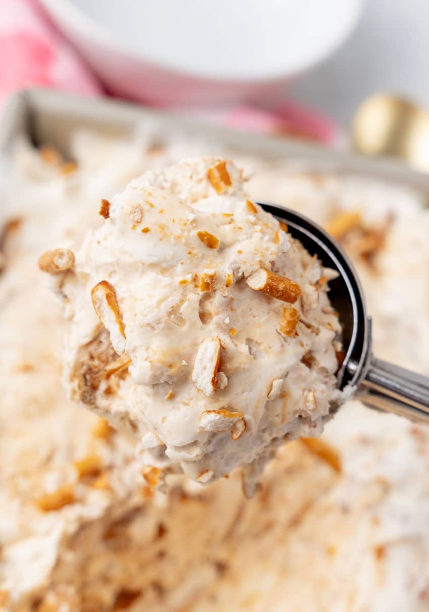 an ice cream scooper holding up a scoop of no churn salted caramel pretzel ice cream