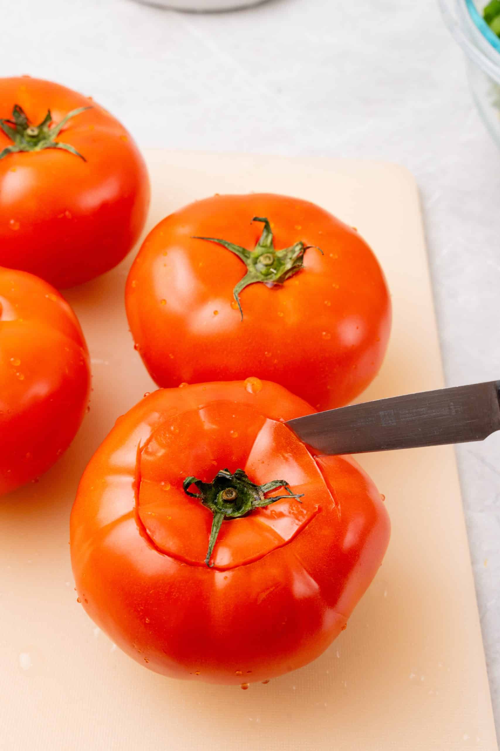 a small knife cutting the tops off ripe tomatoes