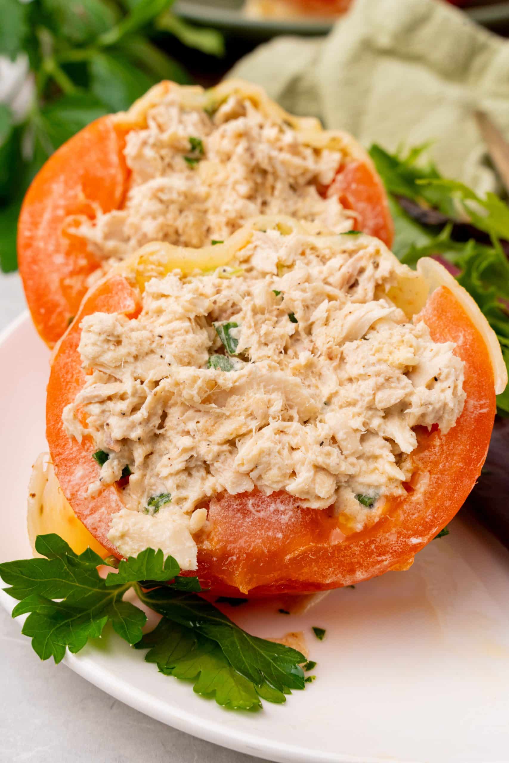 two cut halves of a tuna melt stuffed tomatoes served on a white plate with salad greens on the side