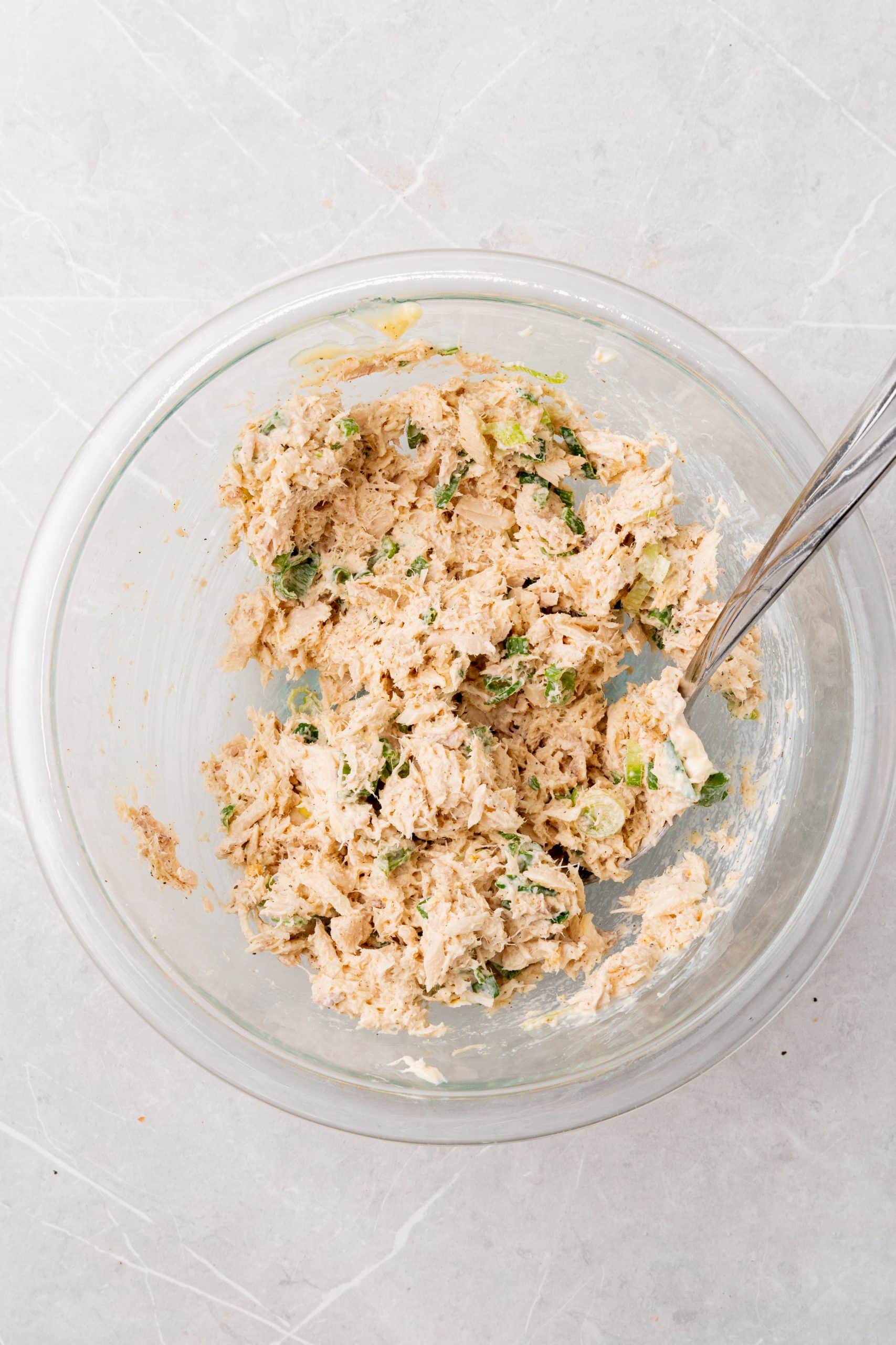 homemade creamy tuna salad mixed together in a glass bowl with a silver fork on the side