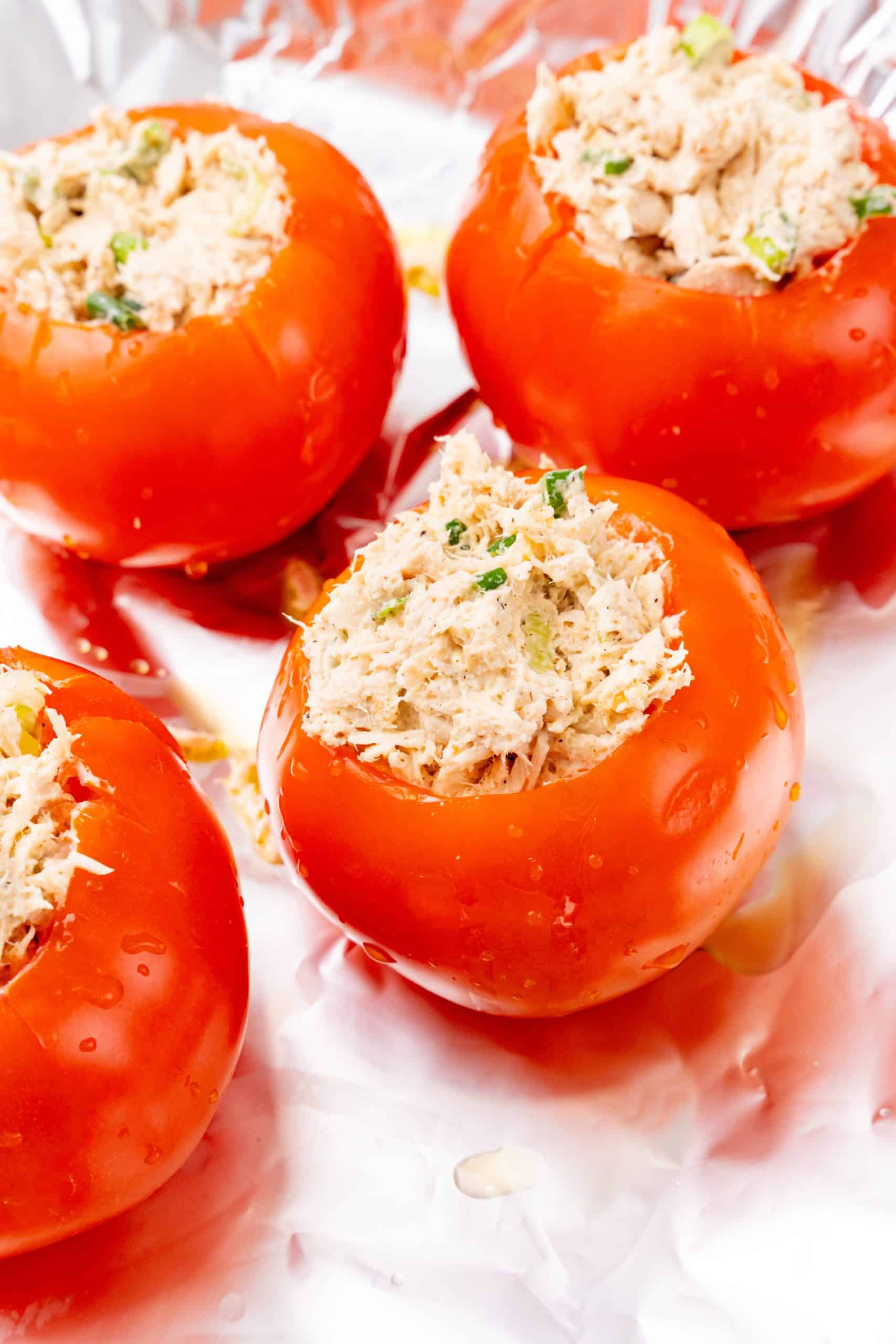 tuna salad stuffed hollowed out tomatoes on a foil lined baking sheet