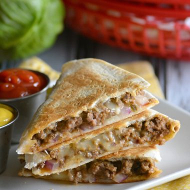 slices of cheeseburger quesadillas stacked on a white plate with small bowls of ketchup & mustard on the side
