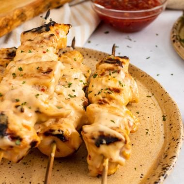 grilled bang bang chicken kabobs arranged in a row on a brown plate