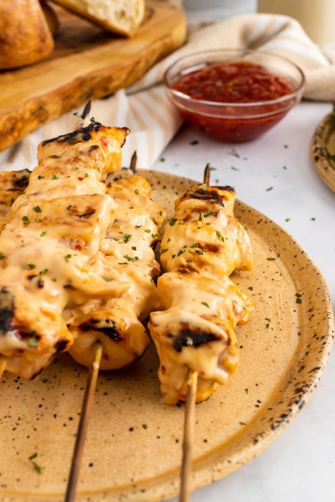 grilled bang bang chicken kabobs arranged in a row on a brown plate