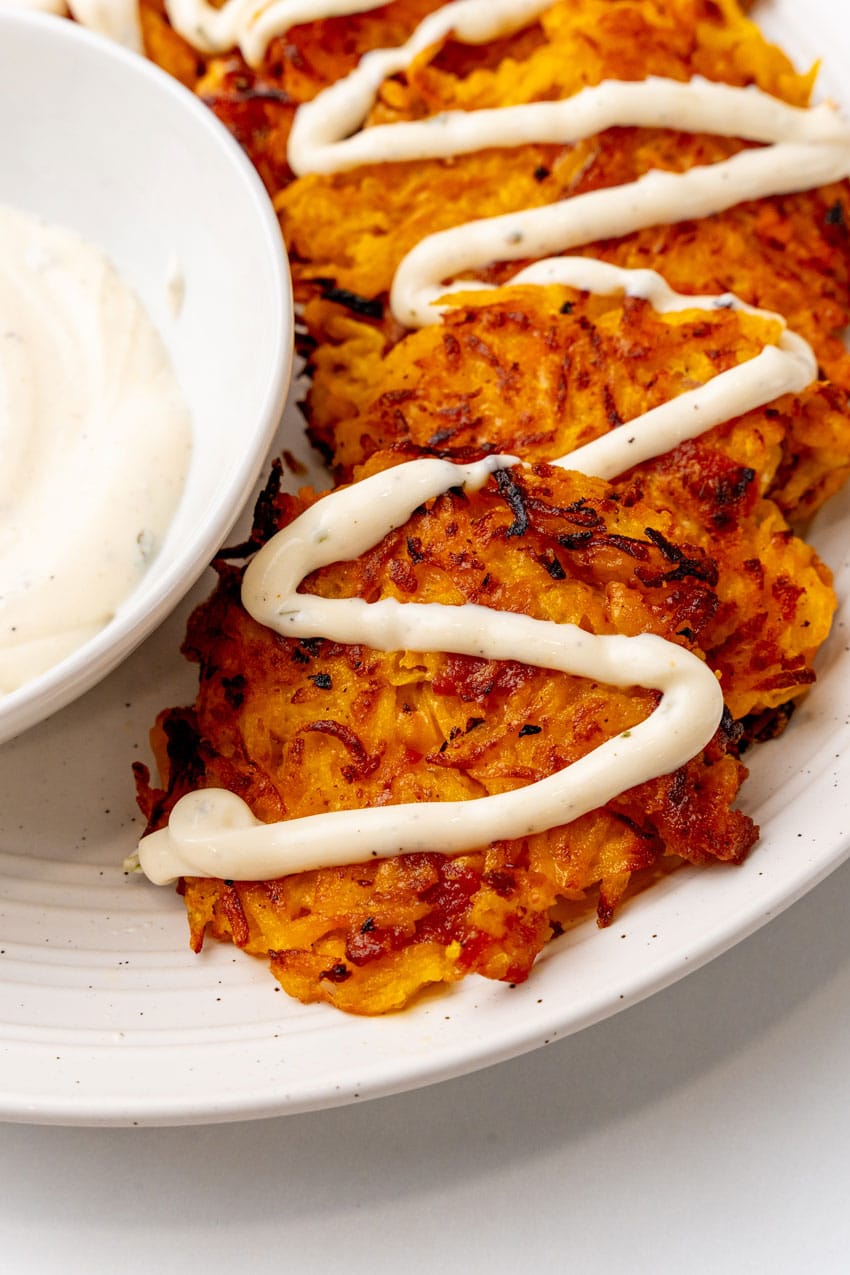 cheesy bacon butternut squash fritters drizzled with ranch crema on a white plate