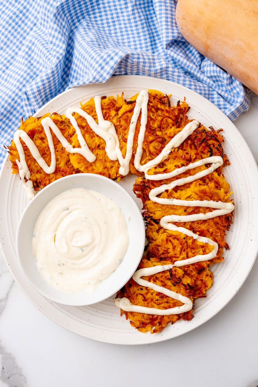 cheesy bacon butternut squash fritters drizzled with ranch crema on a white plate