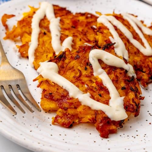 cheesy bacon butternut squash fritters drizzled with ranch crema on a white plate