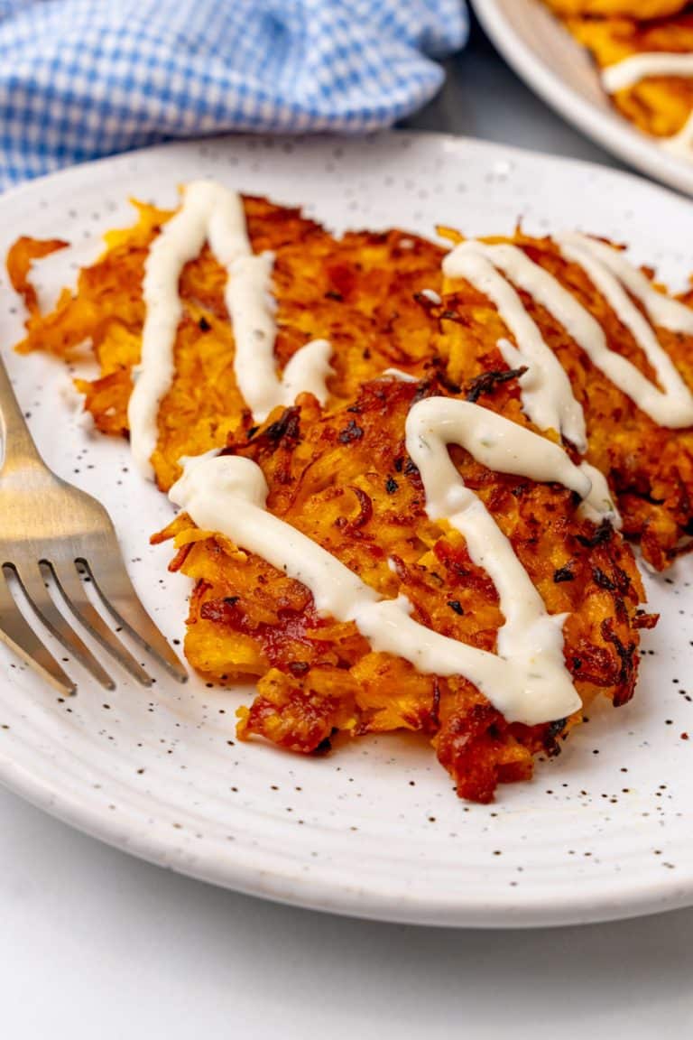 cheesy bacon butternut squash fritters drizzled with ranch crema on a white plate