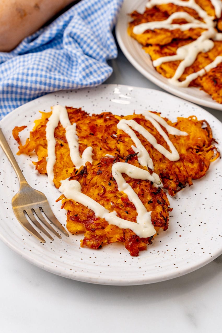 cheesy bacon butternut squash fritters drizzled with ranch crema on a white plate