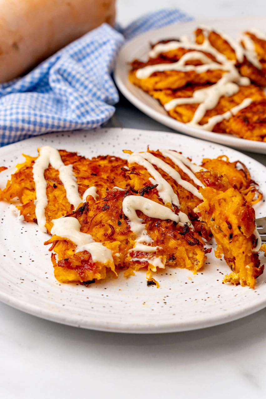 cheesy bacon butternut squash fritters drizzled with ranch crema on a white plate