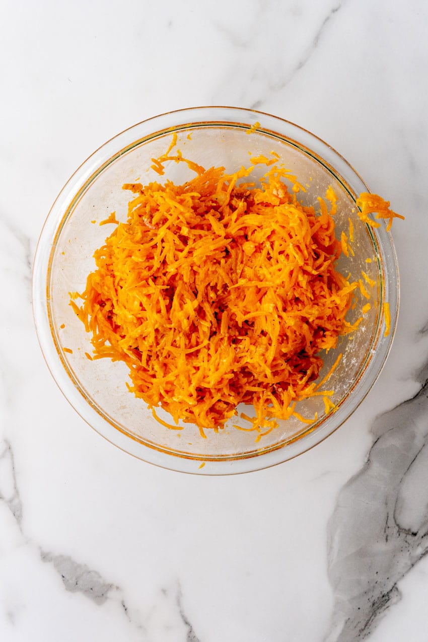 bacon, shredded cheese, and butternut squash mixed together in a glass mixing bowl