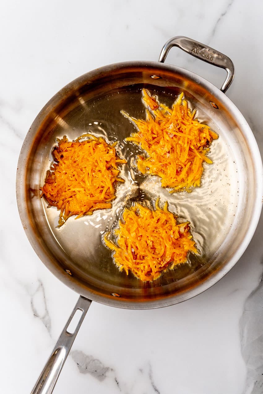 butternut squash fritters frying in hot oil in a metal skillet