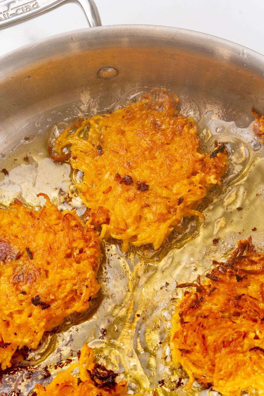 butternut squash fritters frying in hot oil in a metal skillet