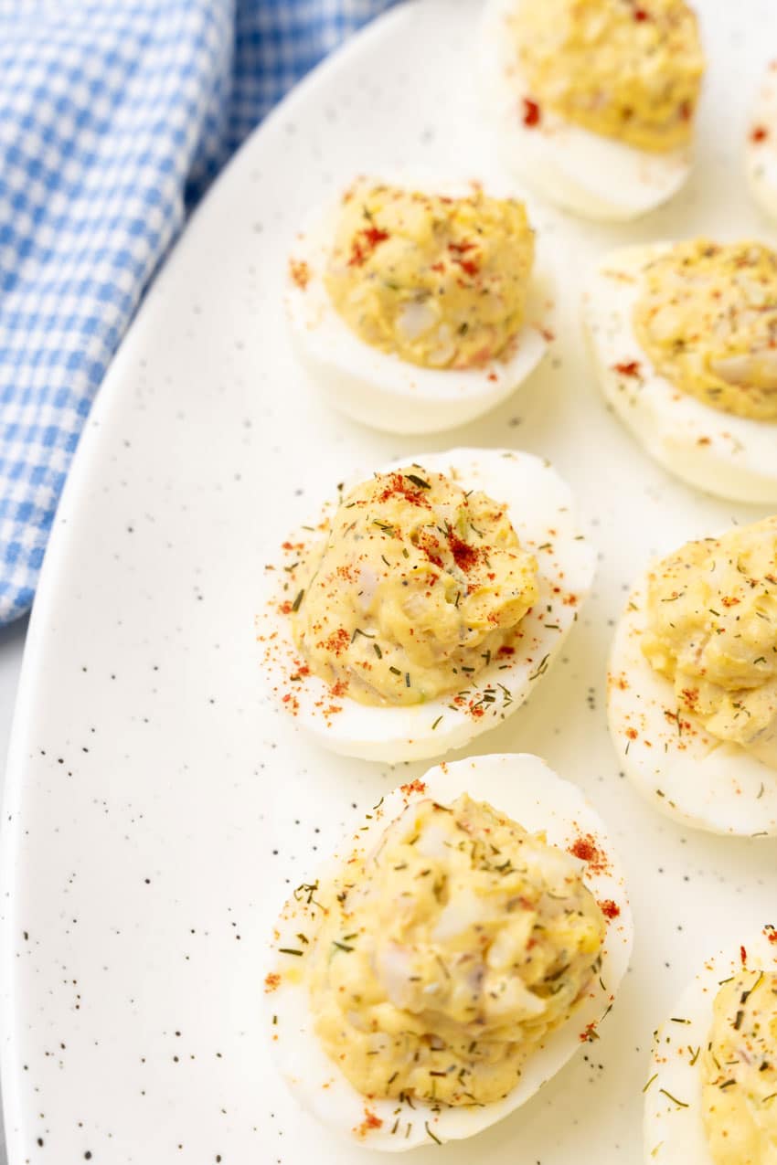 creamy crab deviled eggs arranged in a row on a white serving platter