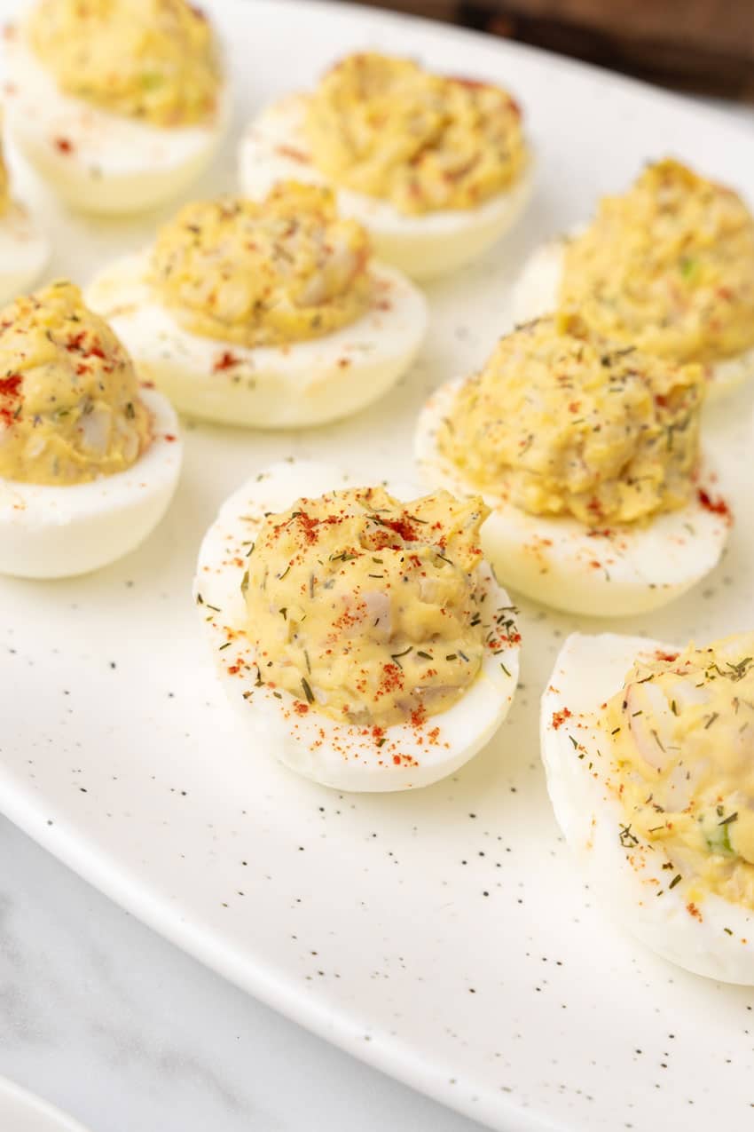 creamy crab deviled eggs arranged in a row on a white serving platter