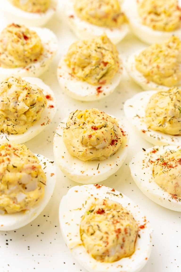 crab stuffed deviled eggs arranged in three rows on a white serving platter