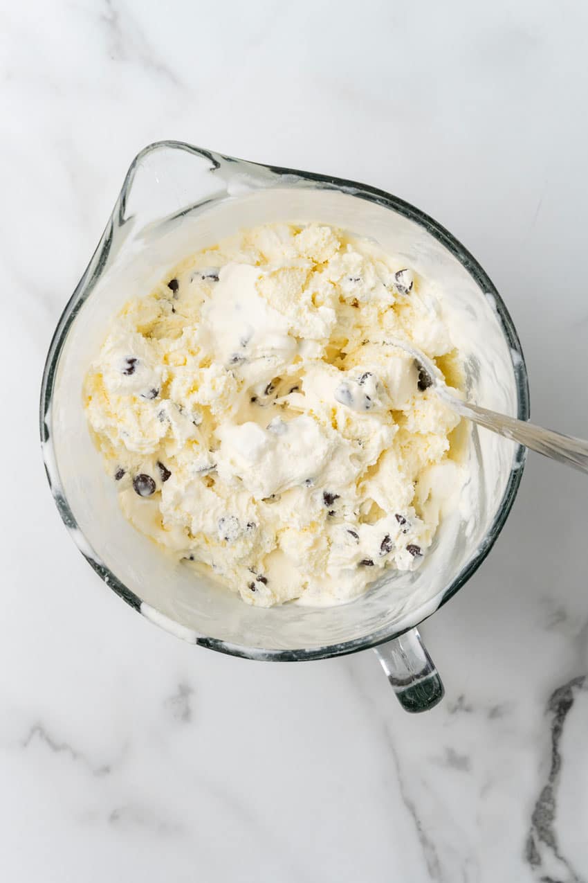 ice cream mixed with chocolate chips and mini marshmallows in a glass mixing bowl