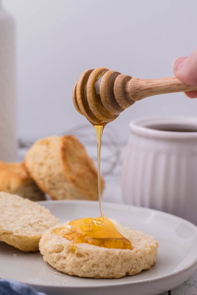 honey being drizzled on a buttermilk biscuit