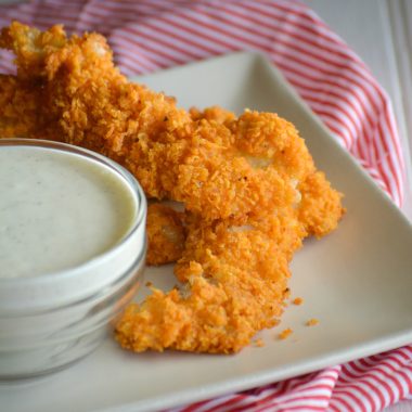 doritos crusted chicken fingers on a white plate with a small bowl of ranch dressing