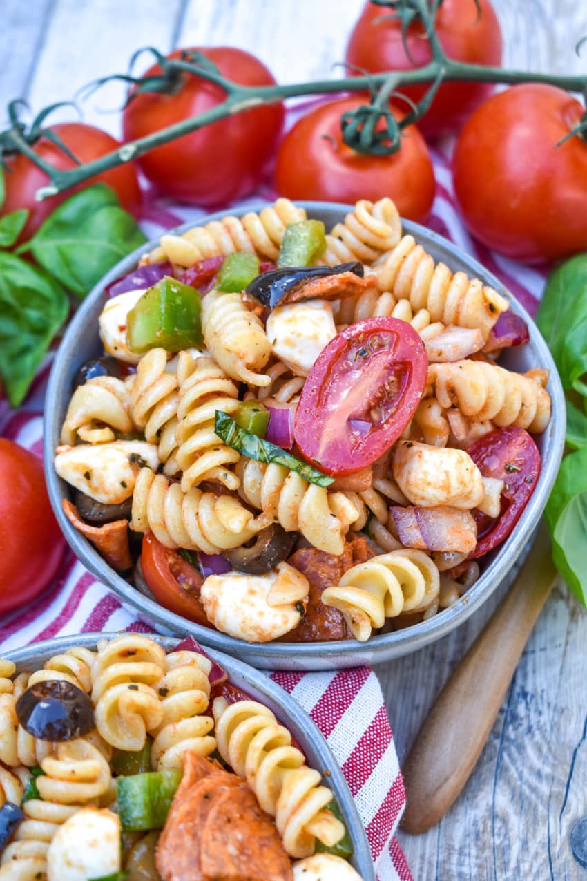 pizza pasta salad in a small gray bowl surrounded by fresh tomatoes