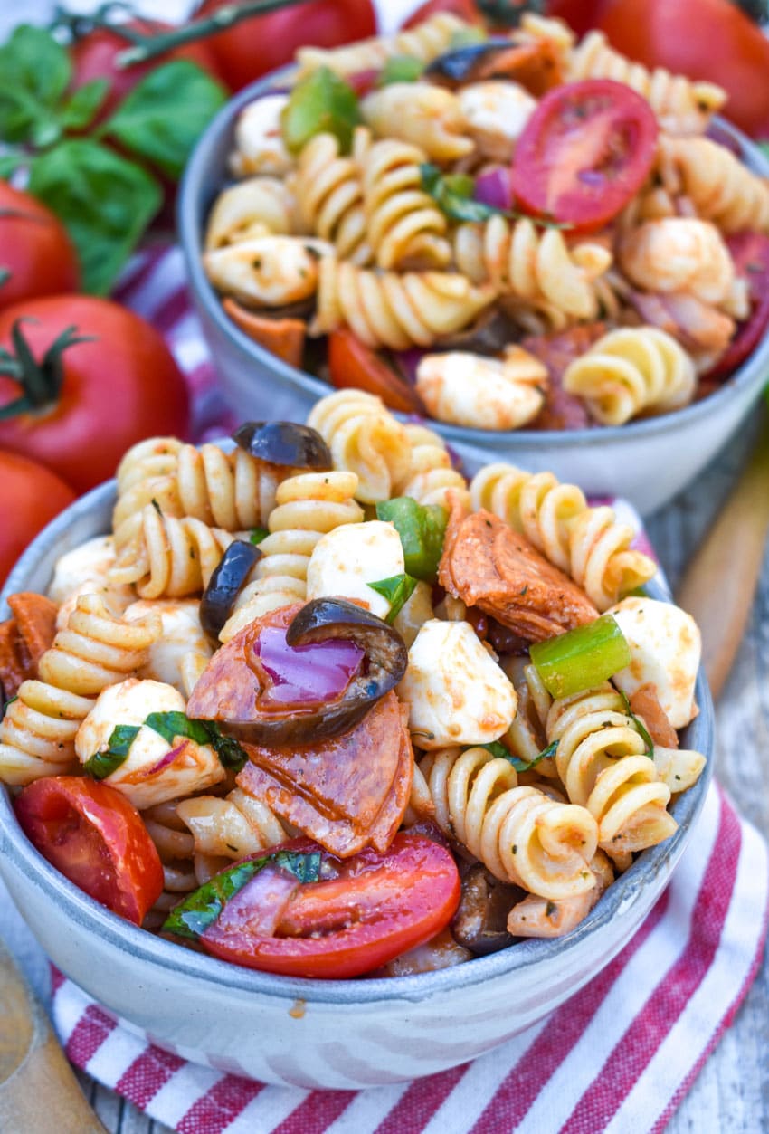pizza pasta salad in a small gray bowl surrounded by fresh tomatoes