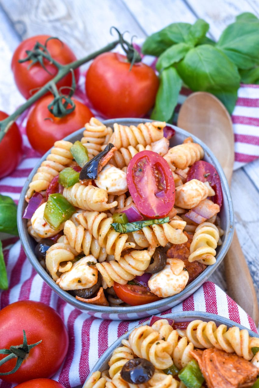 pizza pasta salad in a small gray bowl surrounded by fresh tomatoes