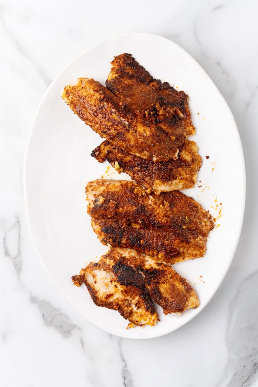 blackened tilapia filets arranged in a row on a white serving platter