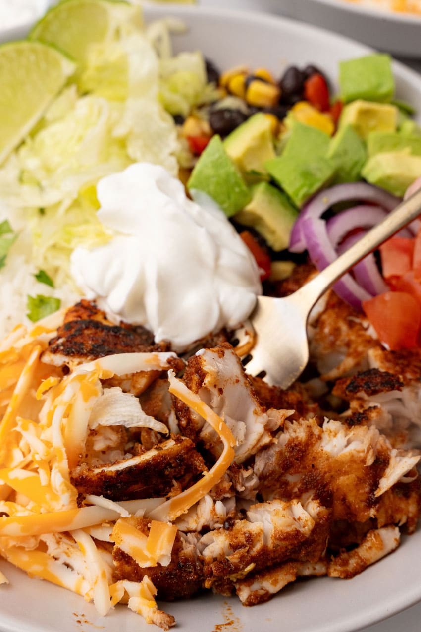 a silver fork digging into a blackened tilapia bowl