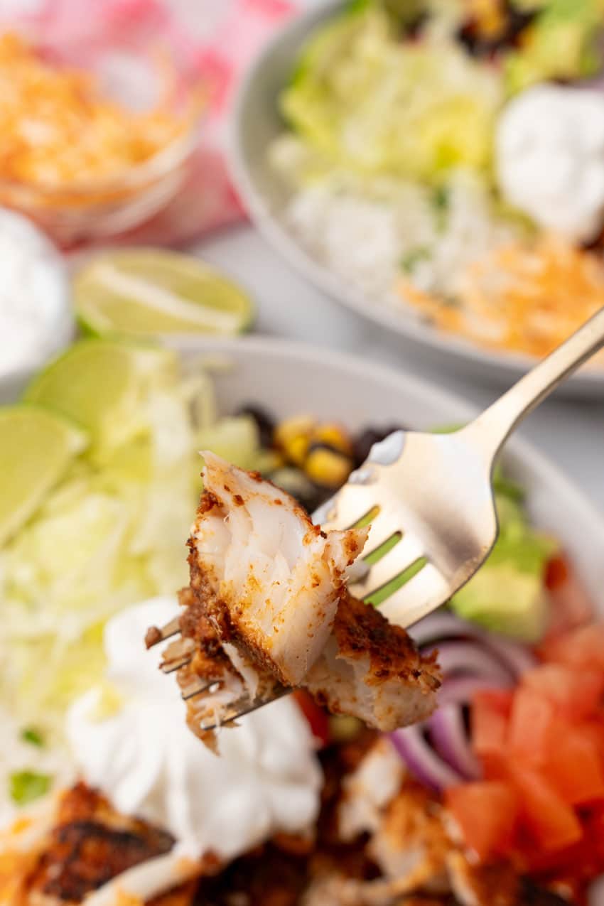 a silver fork lifting up a piece of blackened tilapia 