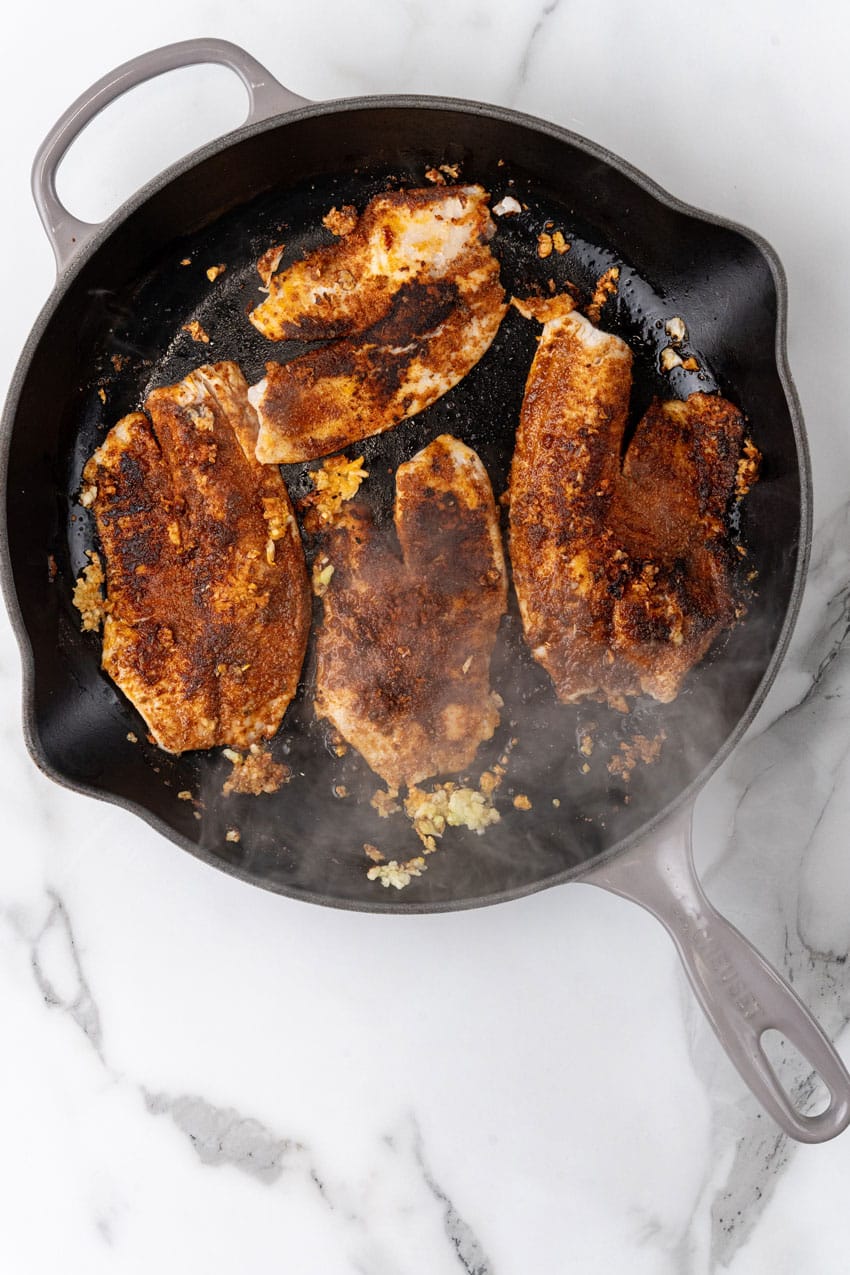 blackened tilapia cooking in a black skillet