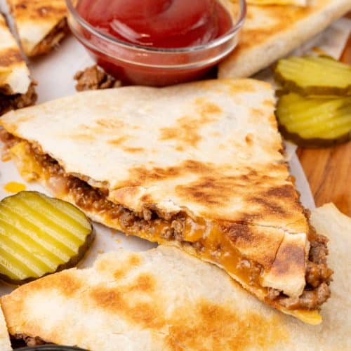 slices of crispy cheeseburger quesadillas stacked on a wooden cutting board