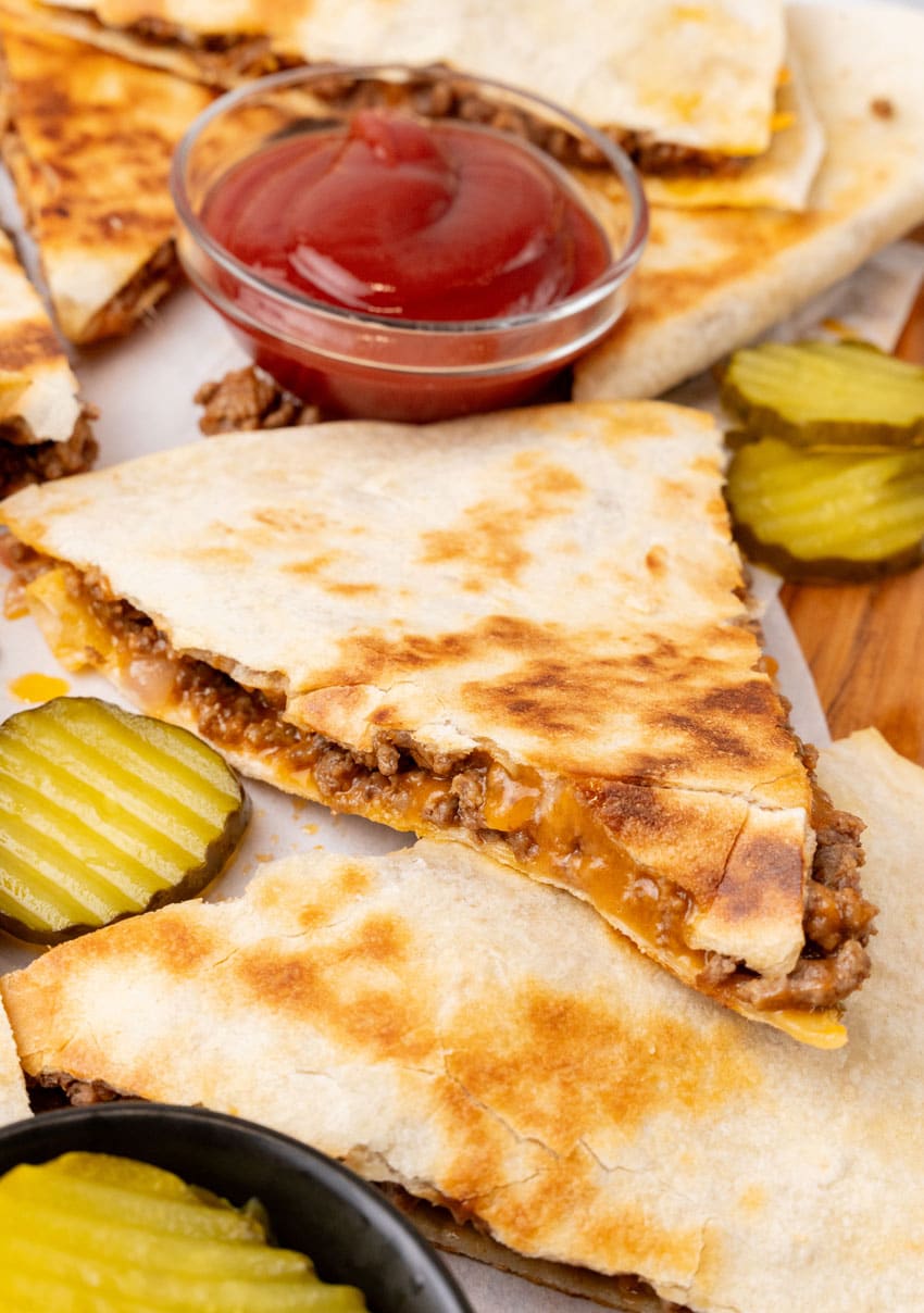 slices of crispy cheeseburger quesadillas stacked on a wooden cutting board