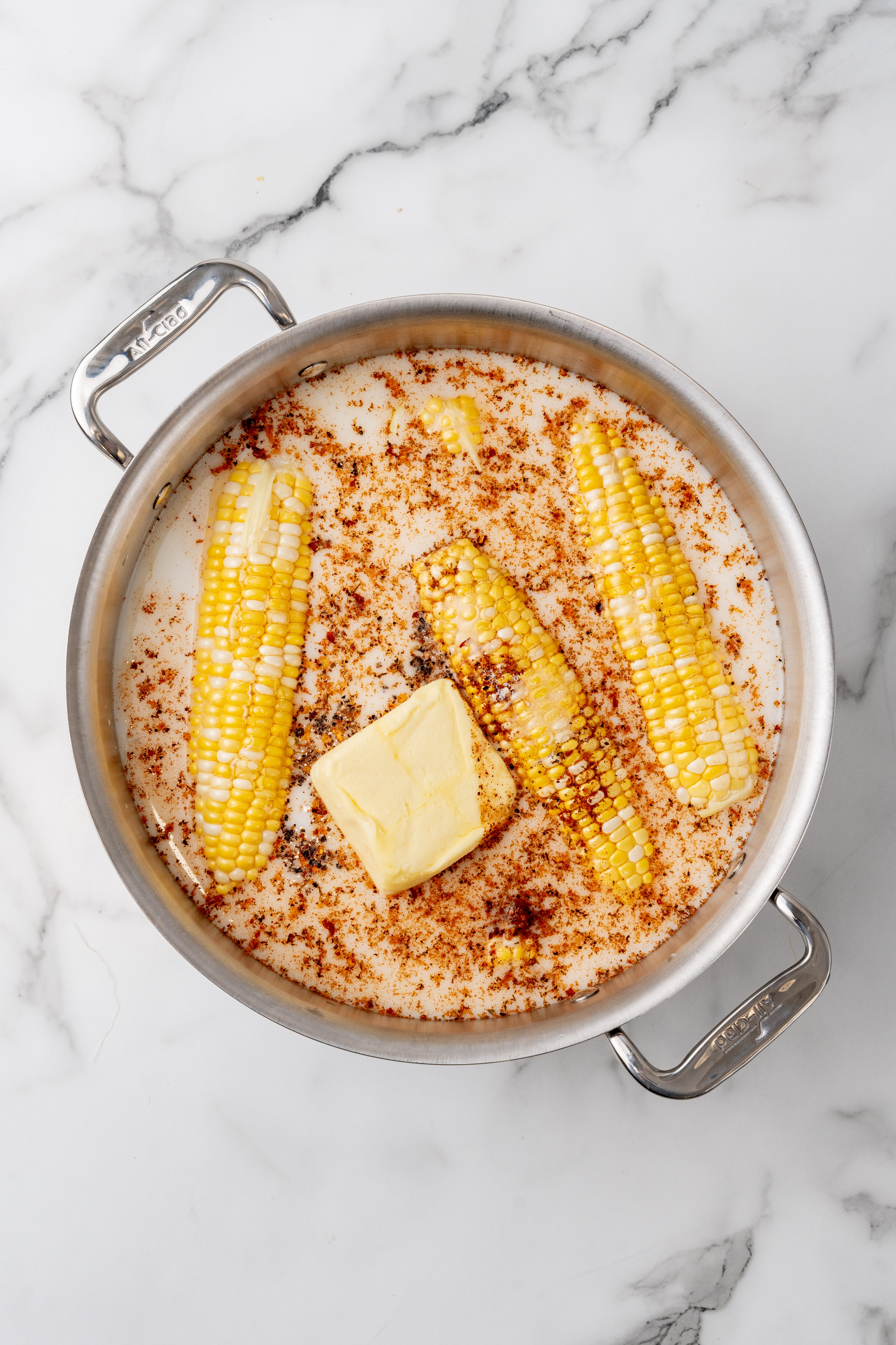 corn cobs and a chunk of butter  in seasoned milk with honey in a silver pot