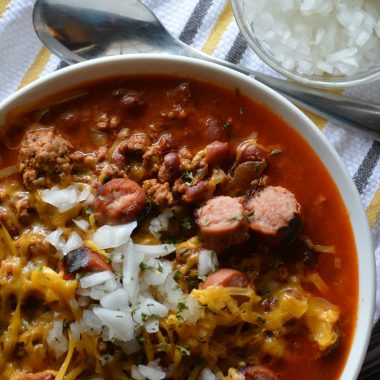 CHILI CHEESE DOG CHILI TOPPED WITH DICED WHITE ONION IN A WHITE BOWL WITH A SILVER SPOON ON THE SIDE