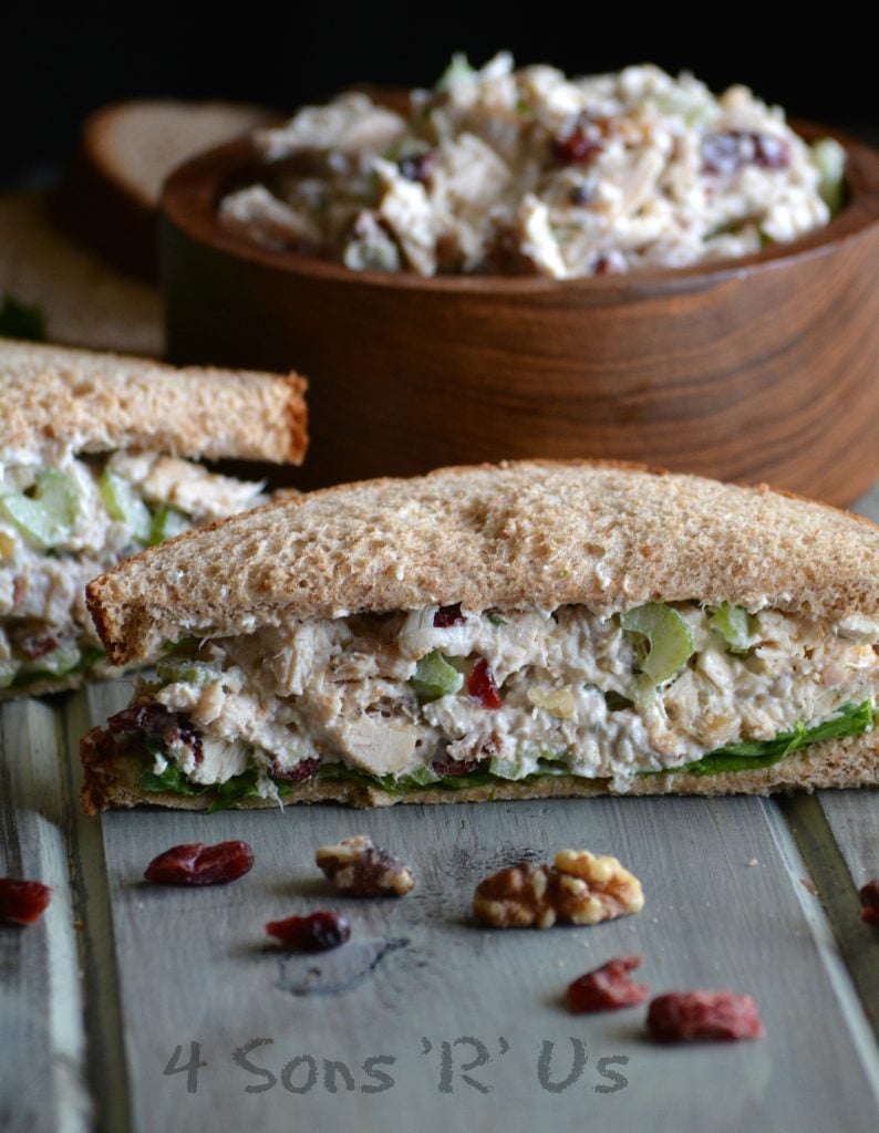 Cranberry Walnut Chicken Salad sandwich cut in half to show the inside with more chicken salad in a wooden bowl shown in the background