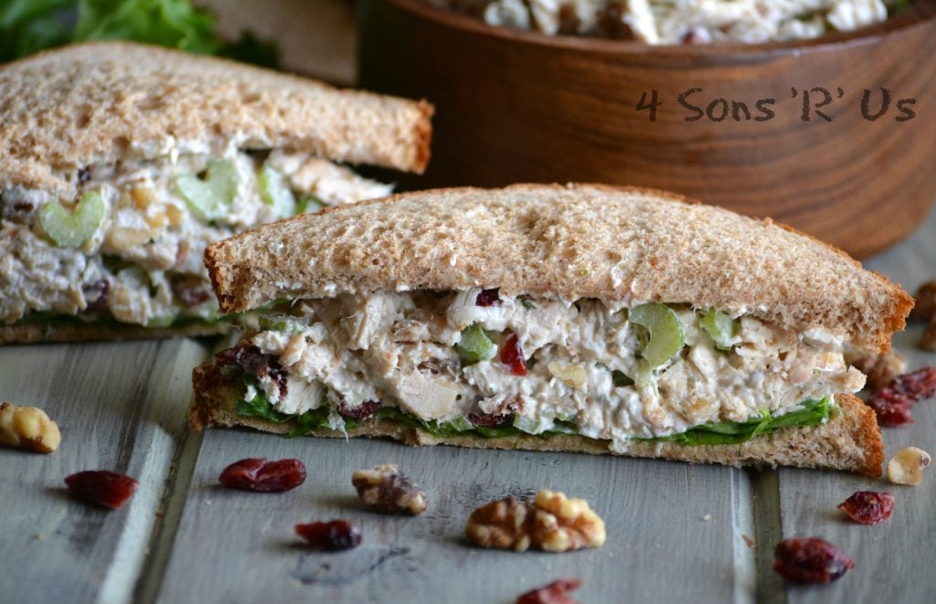 Cranberry Walnut Chicken Salad sandwich cut in half to show the inside with more chicken salad in a wooden bowl shown in the background