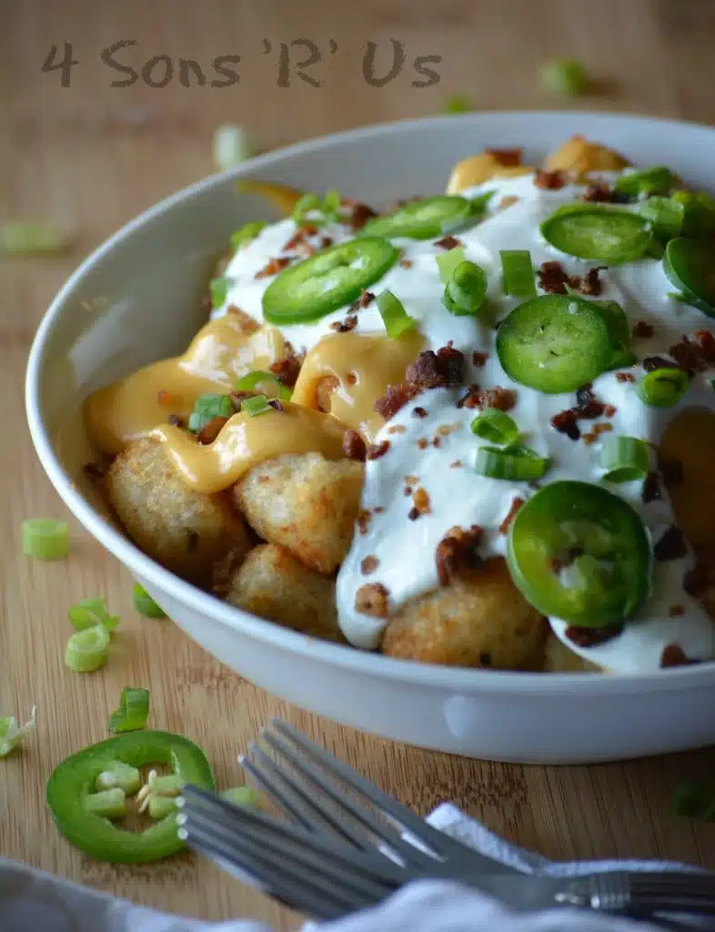 CRISPY TATER TOTS TOPPED WITH CHEESE SAUCE, SOUR CREAM, AND JALAPENO SLICES IN A WHITE BOWL