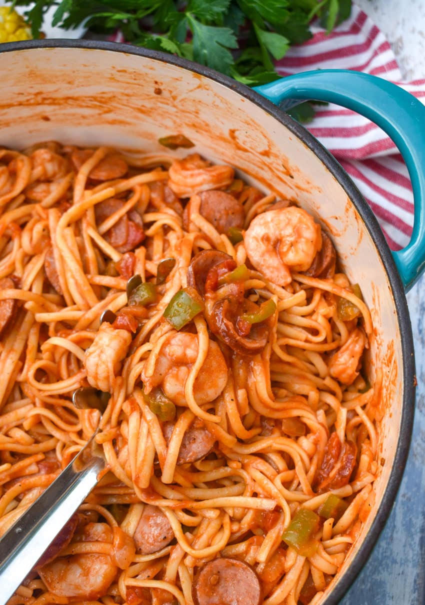 a silver spoon scooping jambalaya pasta out of a large blue pot