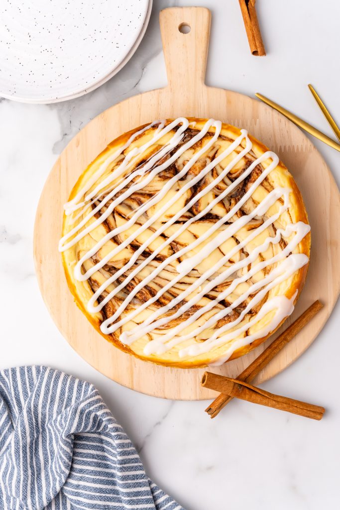 cinnamon bun cheesecake drizzled with cream cheese icing on a wooden cutting board