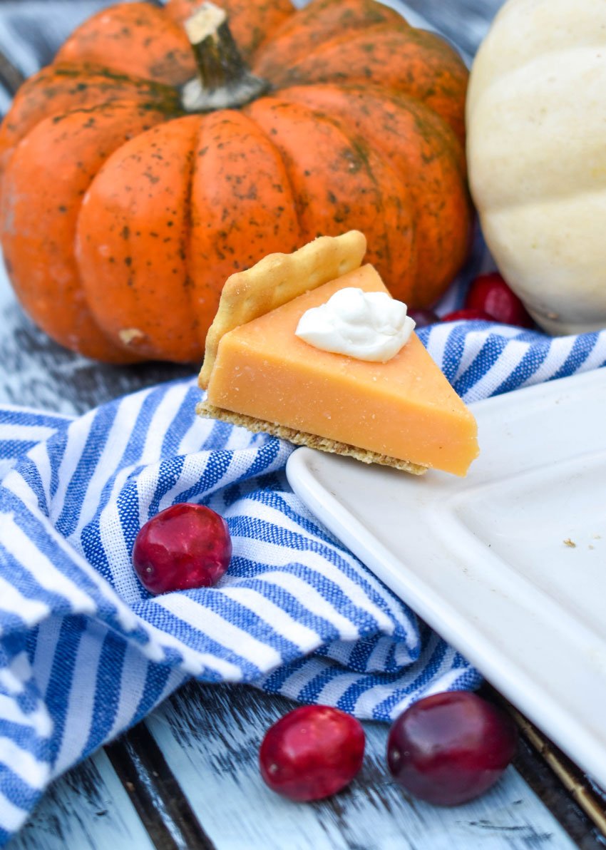 a cheese and cracker pumpkin pie bite resting on the edge of a white serving platter