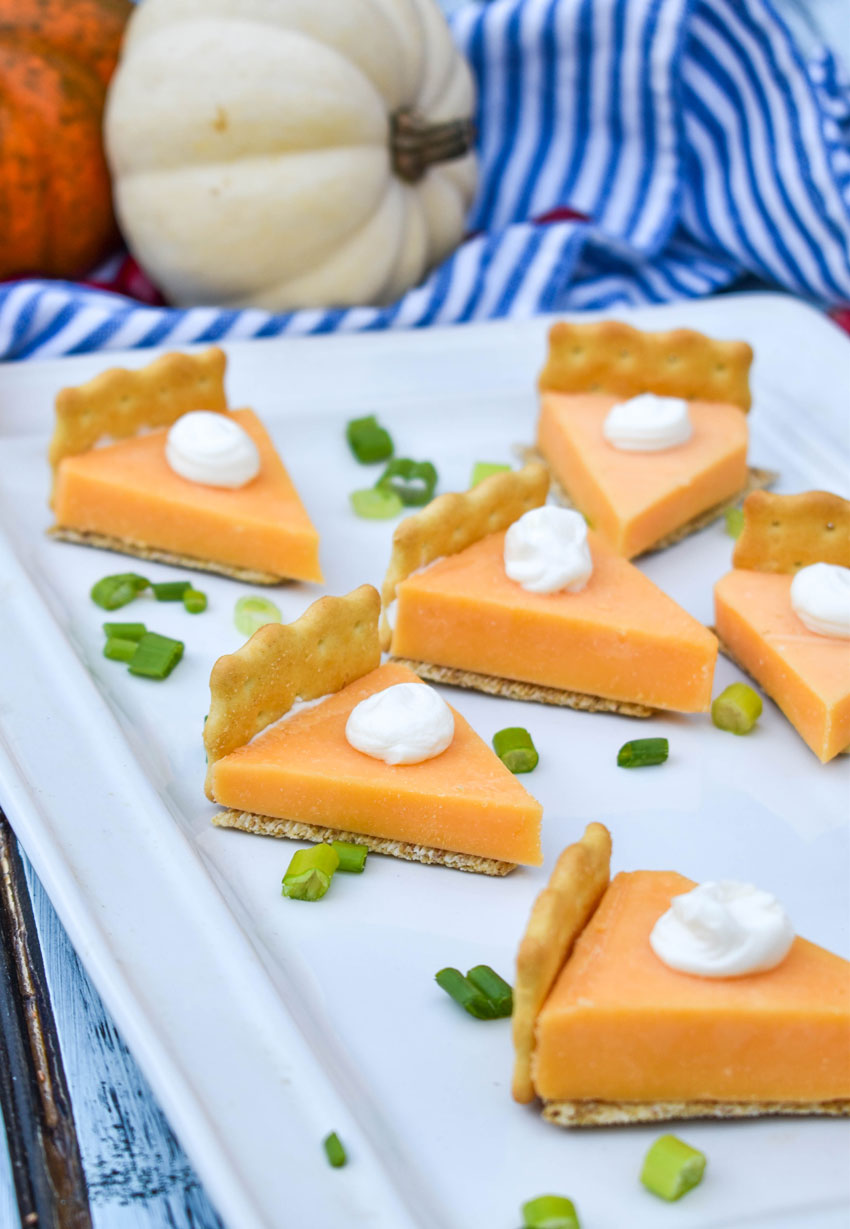 holiday cheese and cracker bites that look like sliced of pumpkin pie on a white serving platter