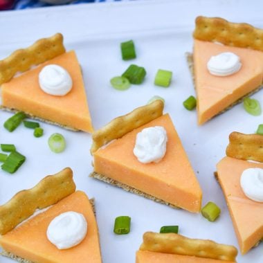 cheese and cracker pumpkin pie bites on a white serving platter with thinly sliced green onions for garnish
