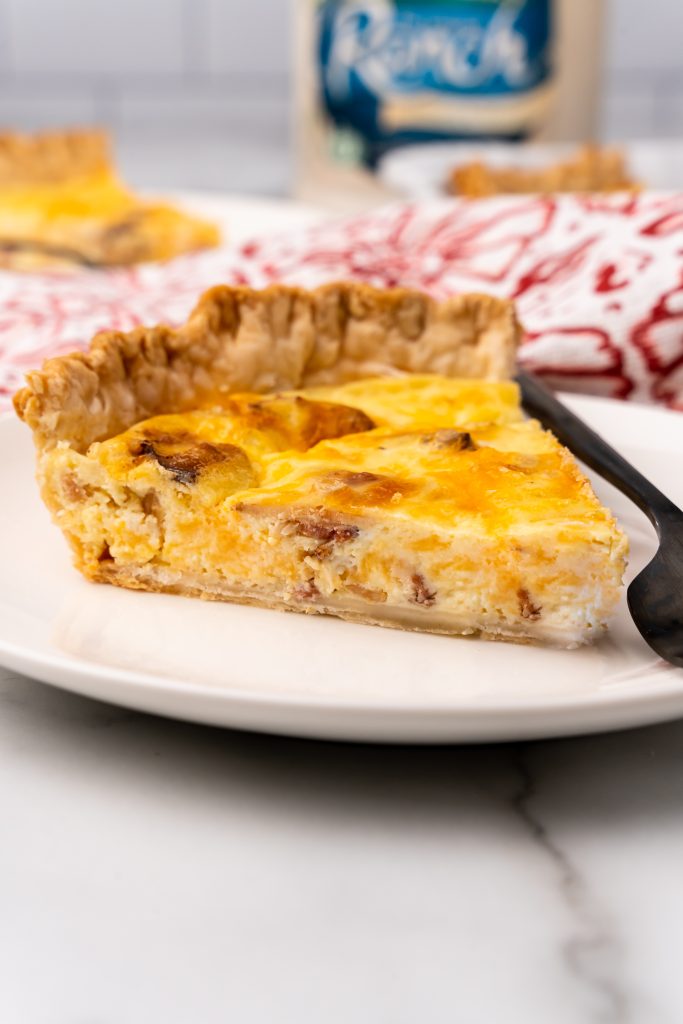 a slice of cheddar bacon ranch quiche on a white plate with a black fork on the side