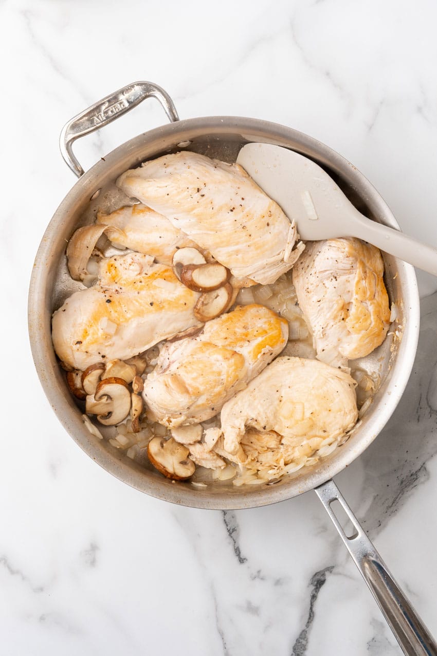 seared chicken breasts with sliced mushrooms and diced onion in a metal skillet