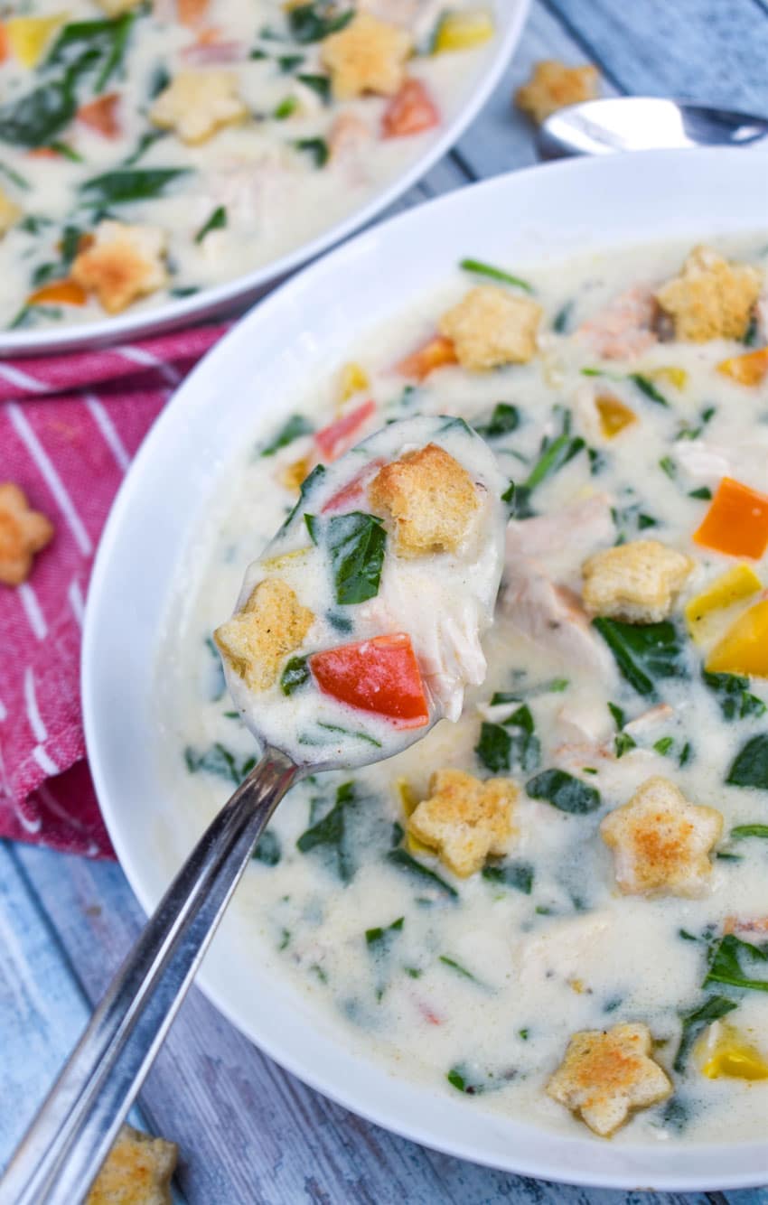a spoon holding up a scoop of creamy chicken soup with homemade croutons