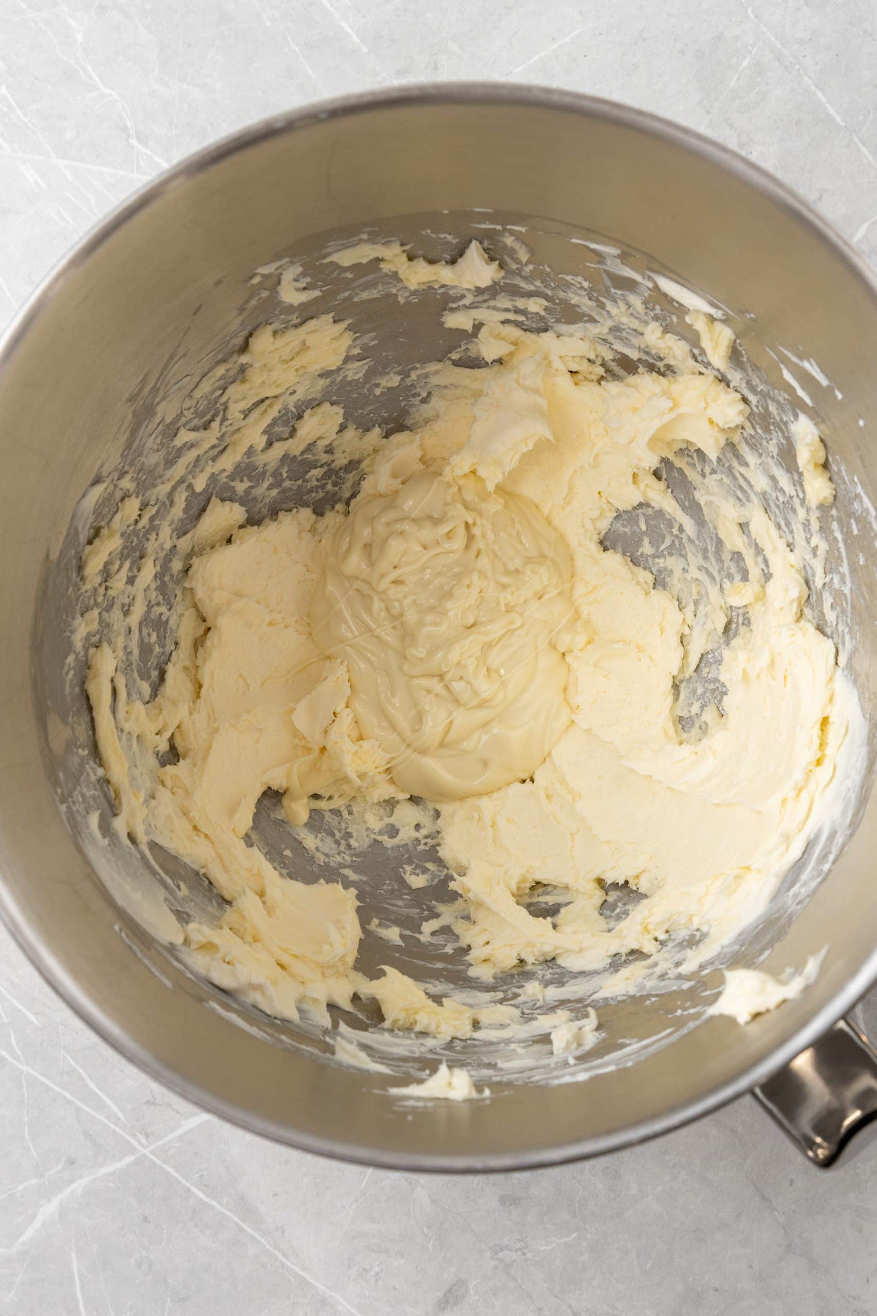 melted white chocolate in frosting batter in a metal mixing bowl