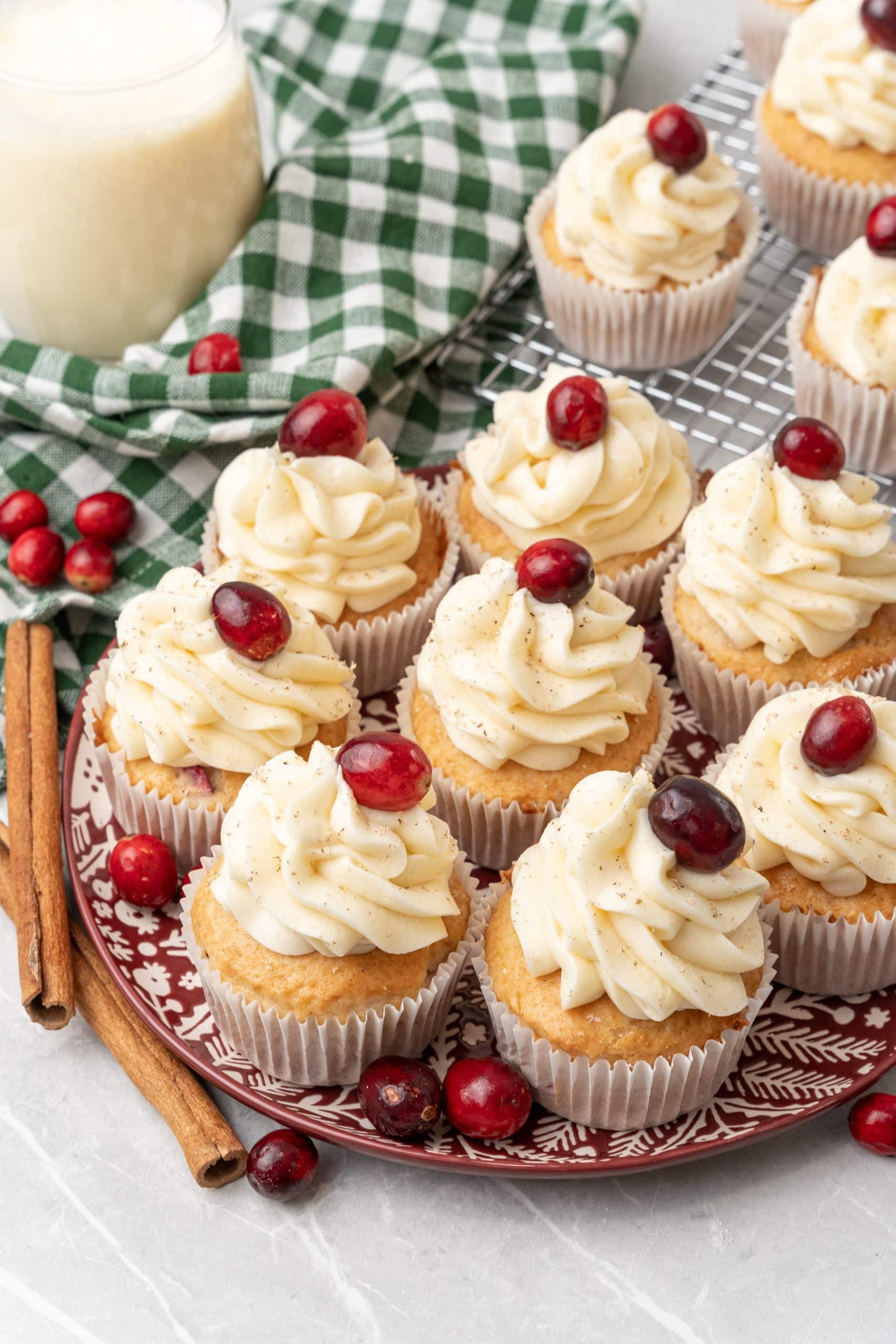 a plate of cranberry eggnog cupcakes surrounded by cinnamon sticks and fresh cranberries