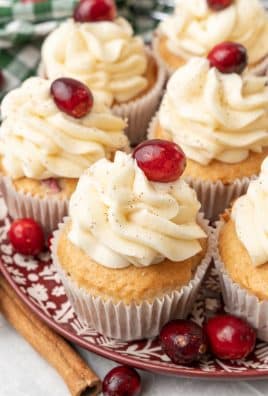a plate of cranberry eggnog cupcakes surrounded by cinnamon sticks and fresh cranberries